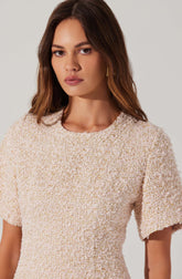 A woman is wearing a cream-colored textured short-sleeve top with a round neckline. The fabric appears woven with a subtle pattern, giving it a slightly rough, nubby appearance.